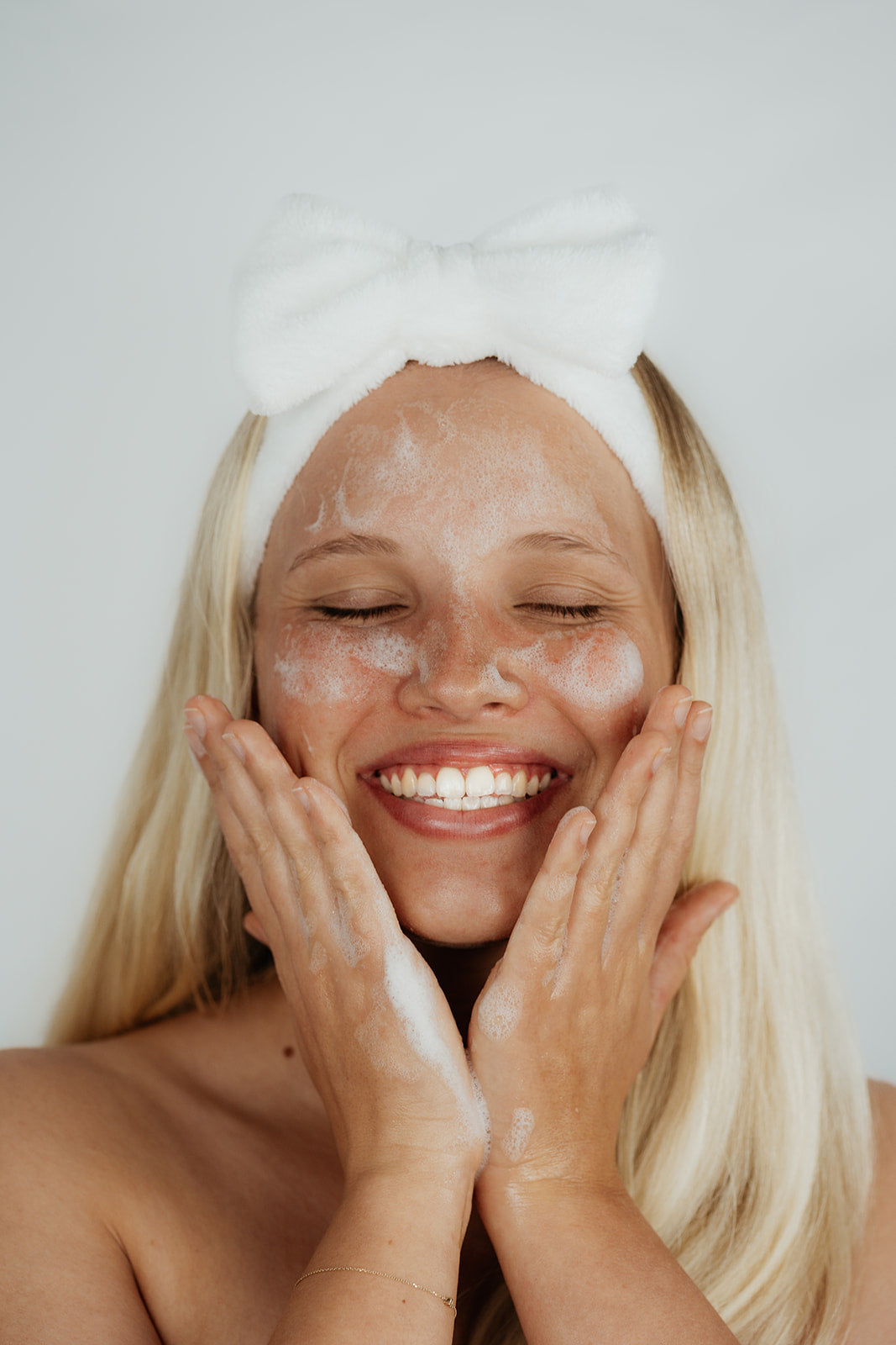 Kindred Skincare headband for your skincare routine all skin types australia - woman girl blonde with no acne pimples washing her face with gel cleanser smiling and happy as she has good skin